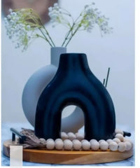 Decorative black vase with a white vase in the background on a light surface.
