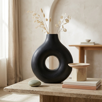 Black vase with dried flowers on a wooden table in a softly lit room.