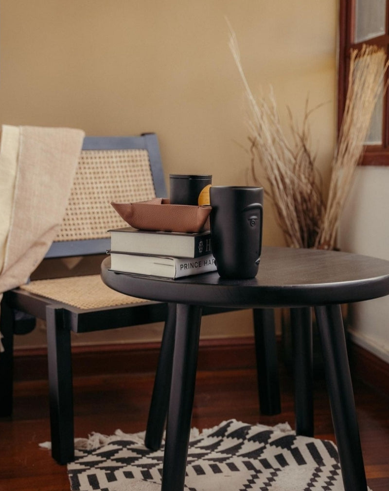 Black side table with books and a mug in a cozy room.