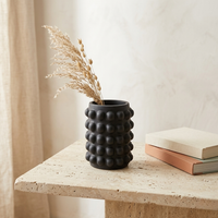 Black textured vase with dried plants on a stone surface