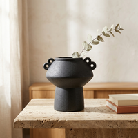 Black ceramic vase with a branch on a wooden table against a neutral background