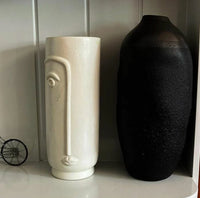 White and black textured vases on a shelf against a tiled wall.