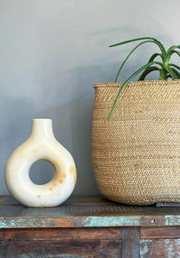 White ceramic vase and woven basket on a wooden surface with a gray wall background