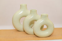 Three ceramic vases with circular designs on a beige surface and background
