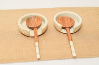 Two wooden spoons with white handles on ceramic coasters on a beige placemat.
