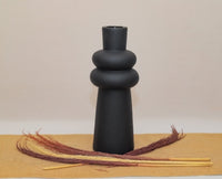 Black ceramic vase on a beige surface with decorative sticks.