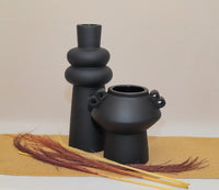 Two black ceramic vases on a beige surface with a blurred background