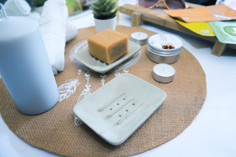 Soap dish with soap on a woven mat, surrounded by various items including a bottle and containers.