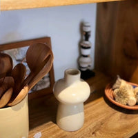 Ceramic vase on a wooden shelf with wooden spoons and a small bowl in the background.