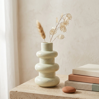 Decorative vase with dried plants on a wooden surface against a beige wall