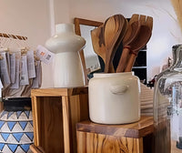 White ceramic container with wooden spoons on a wooden shelf in a store setting.