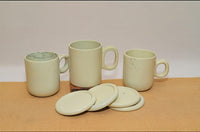 Set of soapstone mugs and coasters on a beige surface with a plain background