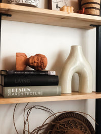 Decorative shelf with books, a vase, and sculptures against a white wall.