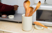Wooden spoons in a white mug on a kitchen counter with a microwave in the background.