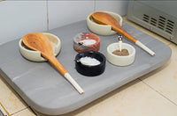 Gray cutting board with bowls of spices and wooden spoons on a tiled kitchen floor.