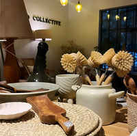 Table setting with ceramic bowls, wooden spoons, and cleaning brushes in a cozy indoor setting.