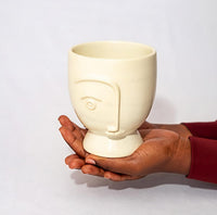 Ceramic cup with face design held by a hand on a light gray background