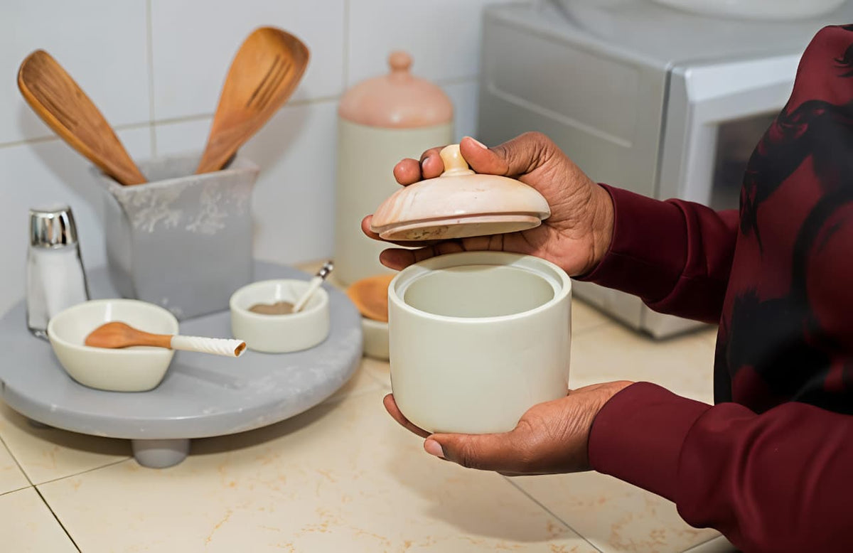 Person holding a white ceramic container with a lid in a kitchen setting.