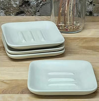 Set of white ceramic soap dishes on a wooden surface with a glass container in the background.